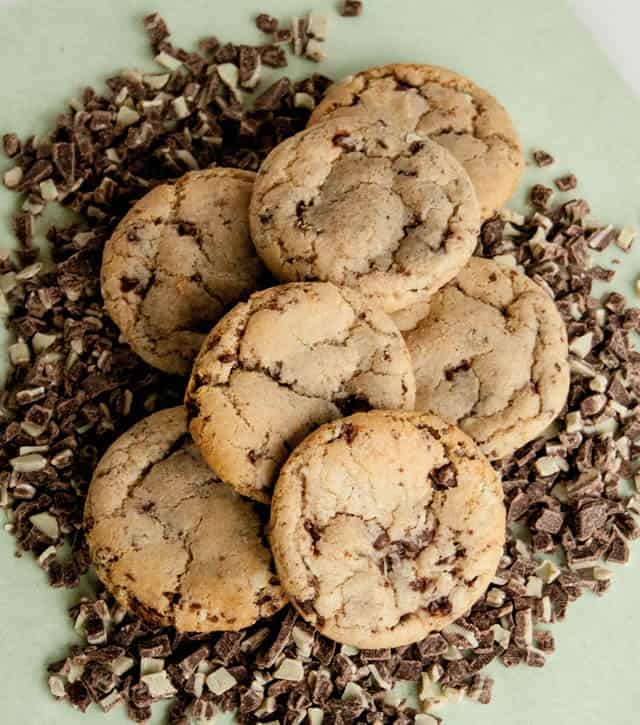 A pile of Andes Mint Chocolate Chip Cookies sitting on a bed of Andes Mint Chocolate Chips from The Merchant Baker
