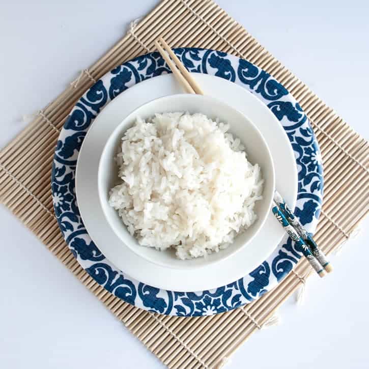 A bowl of Perfect White Rice presented on a plate with chopsticks from themerchantbaker.com