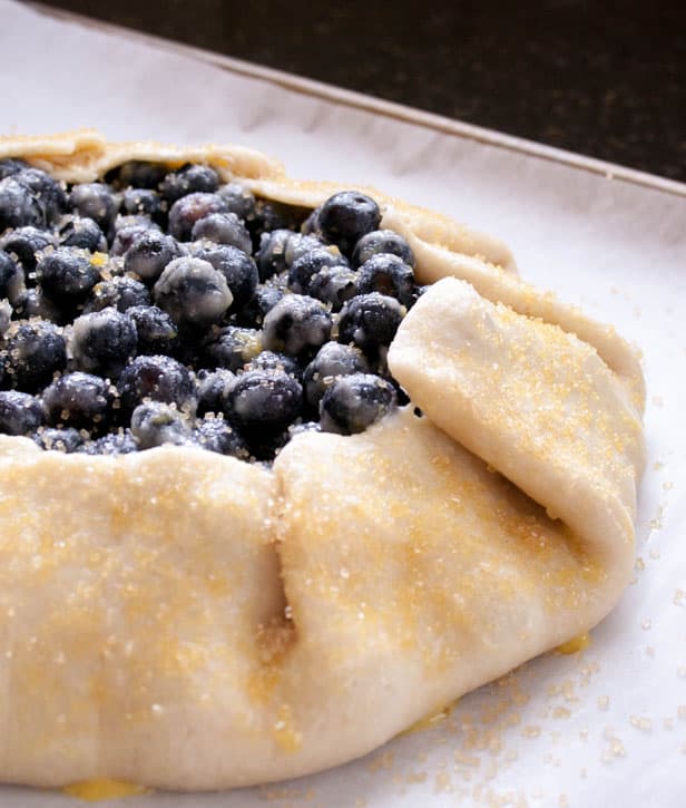 A closeup image of dough for Blueberry Galette wrapped around blueberries and coated with raw sugar from themerchantbaker.com