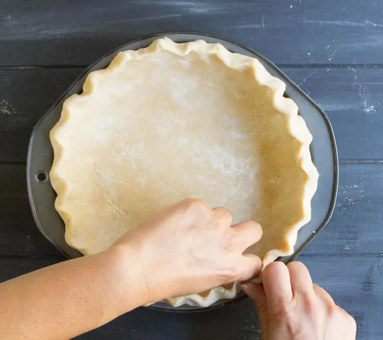 Hands fluting the edge of the Easy All Butter Pie Crust before baking from themerchantbaker.com