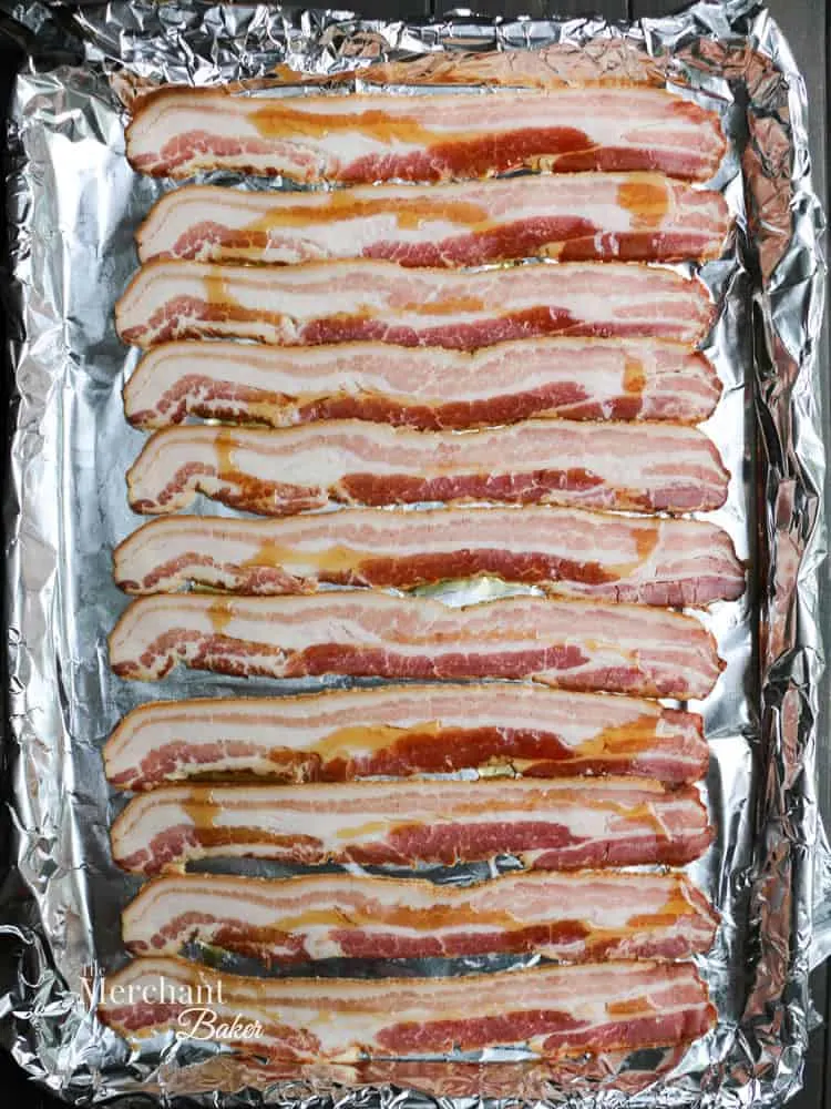 Raw bacon on a baking sheet to make Brown Sugar Maple Glazed Bacon from themerchantbaker.com