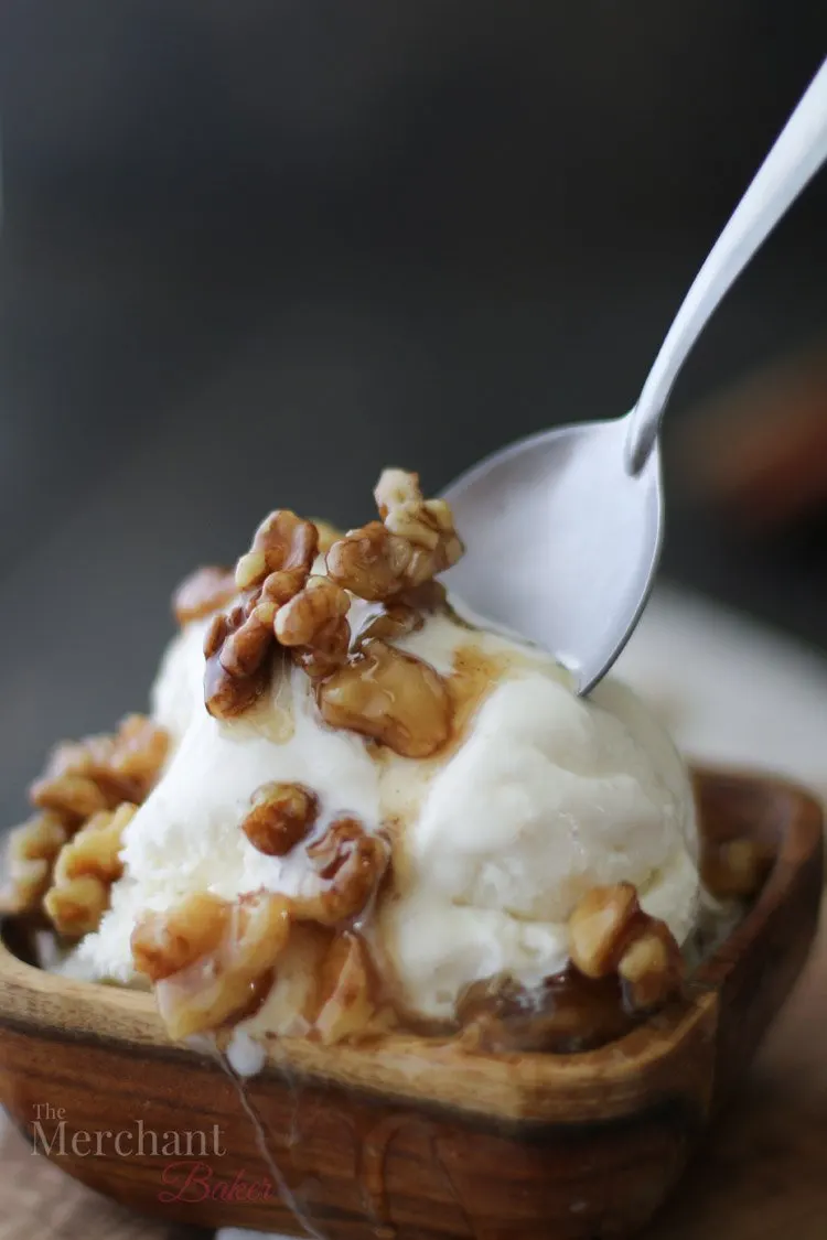 Spoon in a scoop of vanilla ice cream in a wooden bowl topped with walnut syrup