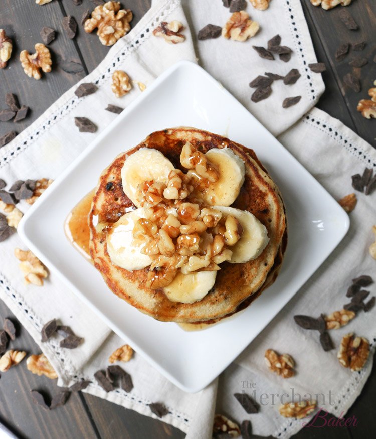 Overhead view of Stack of Oatmeal Chocolate Chip Banana Pancakes topped with sliced bananas and walnut syrup