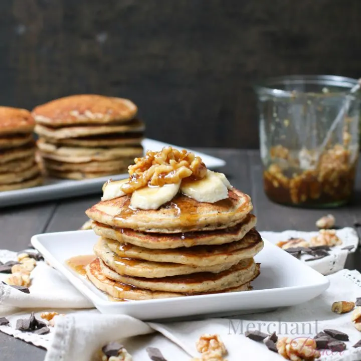 Stack of Oatmeal Chocolate Chip Banana Pancakes topped with sliced bananas and walnut syrup from themerchantbaker.com