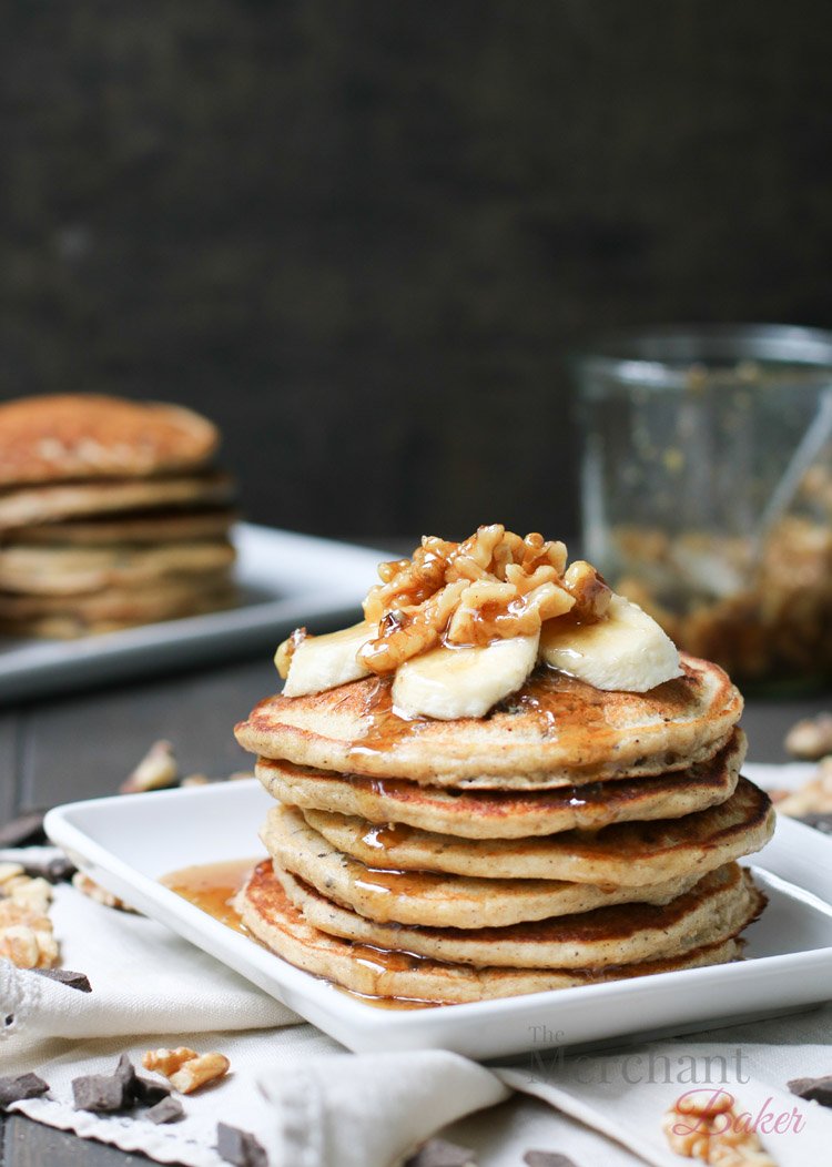 Stack of Oatmeal Chocolate Chip Banana Pancakes topped with sliced bananas and walnut syrup