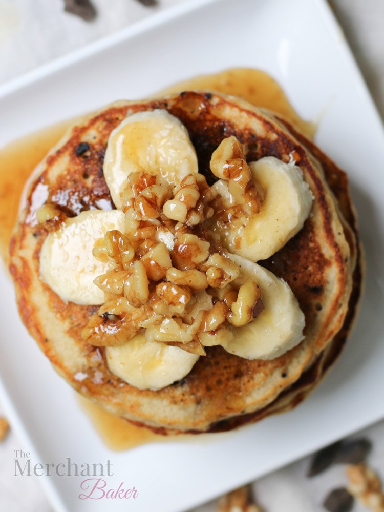 Overhead view of Stack of Oatmeal Chocolate Chip Banana Pancakes topped with sliced bananas and walnut syrup