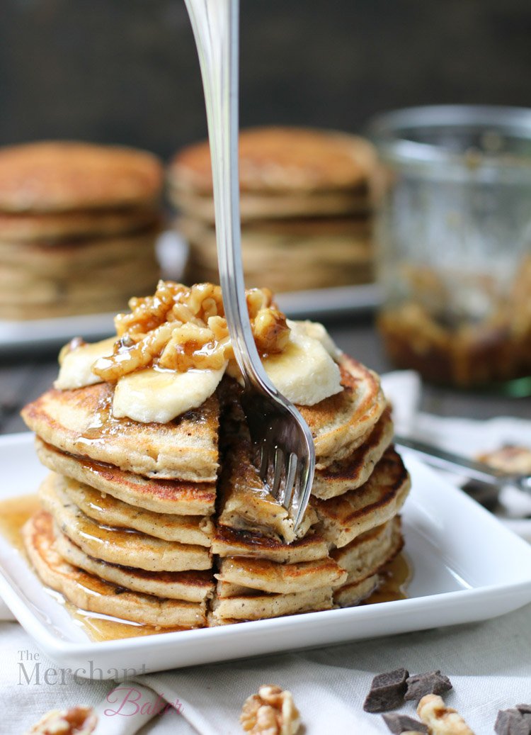 Stack of Oatmeal Chocolate Chip Banana Pancakes speared with a fork topped with sliced bananas and walnut syrup