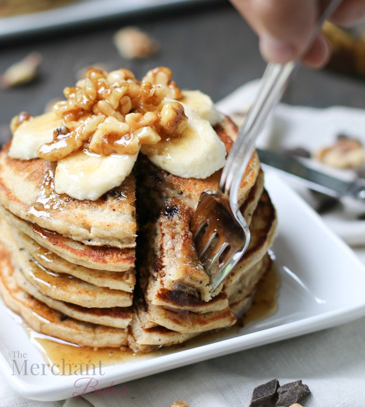 Stack of Oatmeal Chocolate Chip Banana Pancakes speared with a fork topped with sliced bananas and walnut syrup