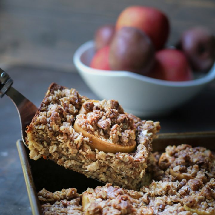 Side photo of a slice of Baked Apple Oatmeal being lifted out of baking pan by themerchantbaker.com