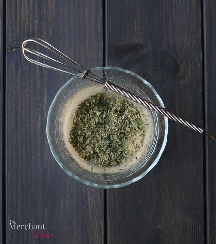 An overhead photo of herbs in a bowl with a whisk to make Low Carb Stuffing Chaffles by themerchantbaker.com