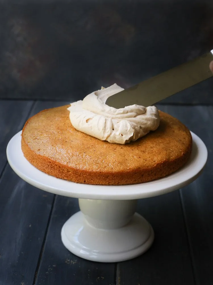A Pumpkin Ale Cake on a pedestal with icing being applied by themerchantbaker.com