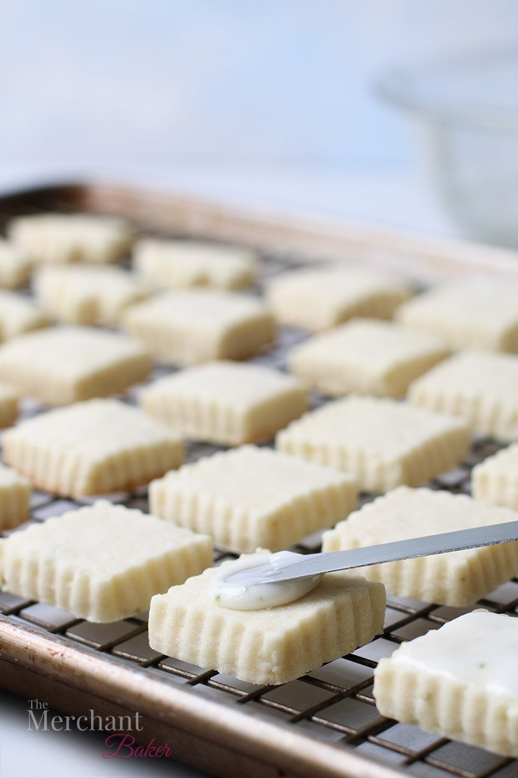 A close up view of icing being spread on a square meltaway cookie