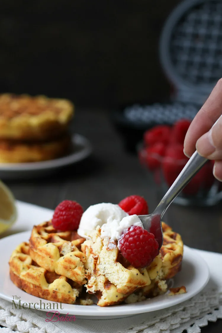 A fork lifting a slice of Lemon Ricotta Poppyseed Chaffles topped with raspberries and a scoop of ricotta by themerchantbaker.com