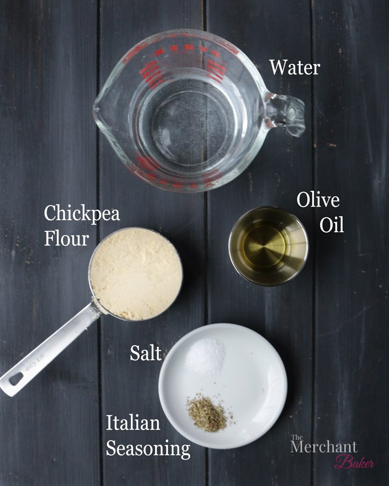 Overhead image of water, chickpea flour, olive oil, salt, and Italian seasoning to make Socca Pizza crust by themerchantbaker.com