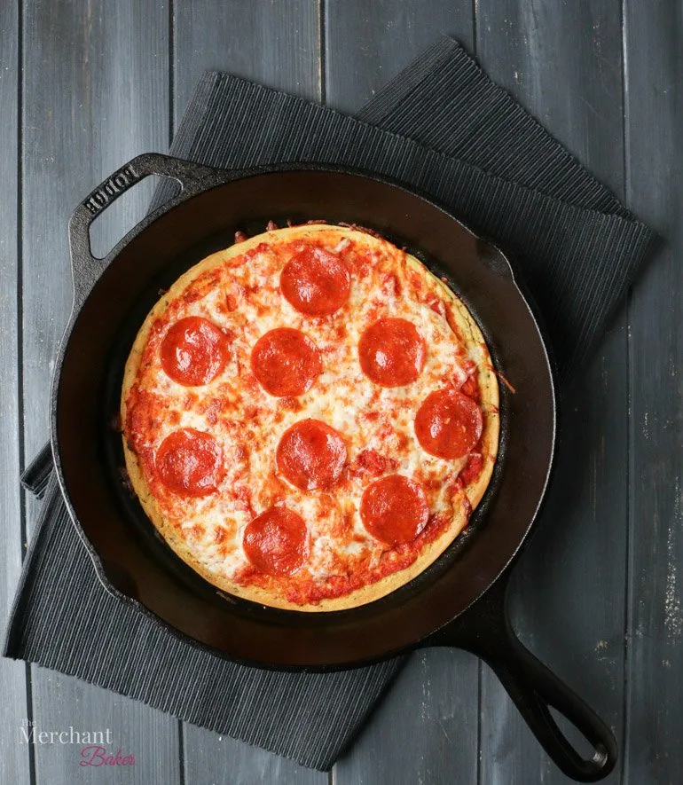 An overhead image of baked pepperoni Socca Pizza in an iron skillet by themerchantbaker.com