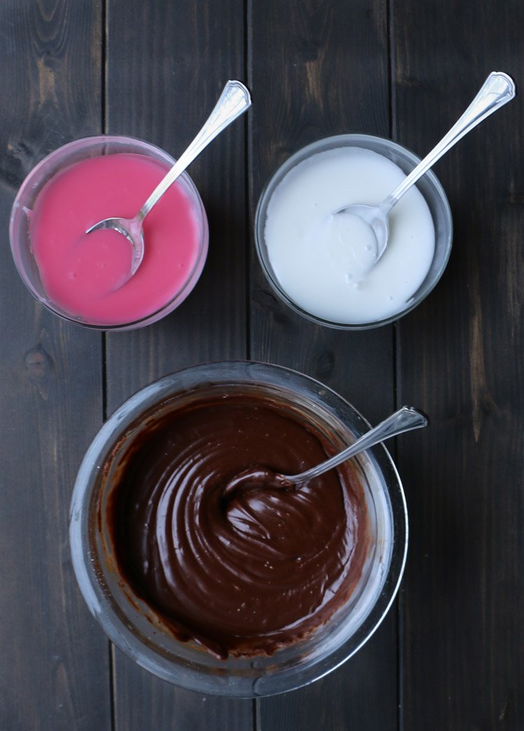 Top view of pink, white, and chocolate icing in bowls by themerchantbakr.com