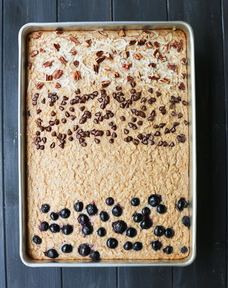 Overhead view of Big Batch Baked Oatmeal in baking pan with rows of blueberries, chocolate chips and pecans and coconut baked on top.