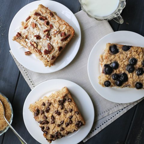 Overhead view of three baked oatmeal squares topped with pecans and coconut, chocolate chips and blueberries