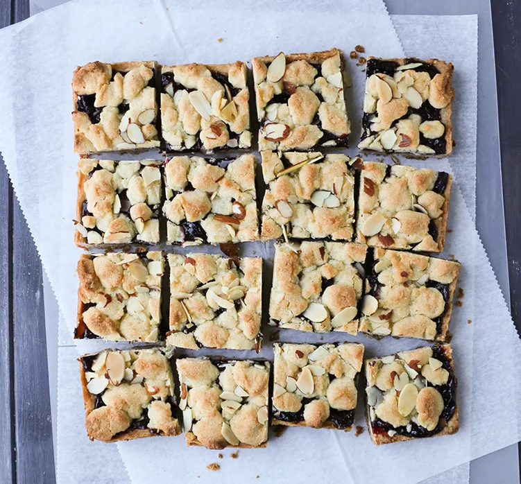Cut squares of Cherry Crumb Bars on parchment paper by thermerchantbaker.com