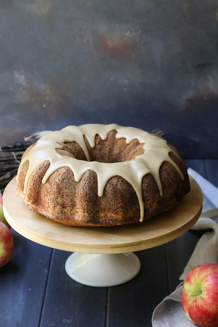 A top angle view of an apple pie bundt cake topped with maple icing by themerchantbaker.com