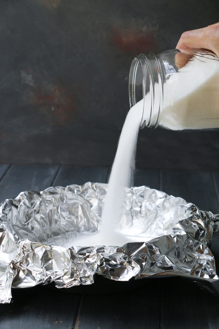 white sugar being poured into a foil lined unbaked pie crust