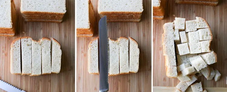 Piles of bread slices on a cutting board being cut into cubes with a bread knife