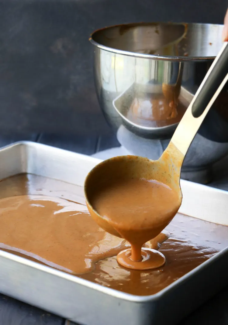 a ladle full of pumpkin pie filling being spooned over gingerbread batter