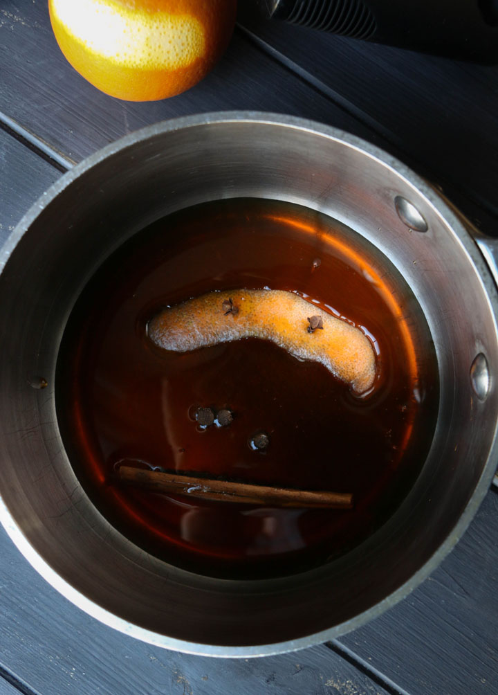 overhead view of orange rind and spices in a sauce pan with maple syrup