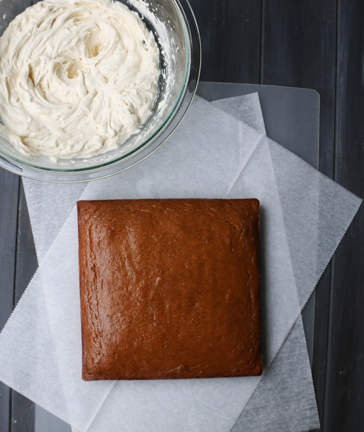 A square crazy pumpkin olive oil cake on parchment paper next to a bowl of frosting