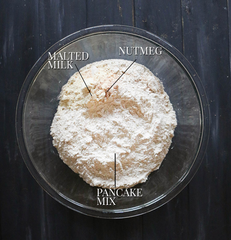 Overhead shot of Kodiak pancake mix, malted milk powder and nutmeg in a glass mixing bowl