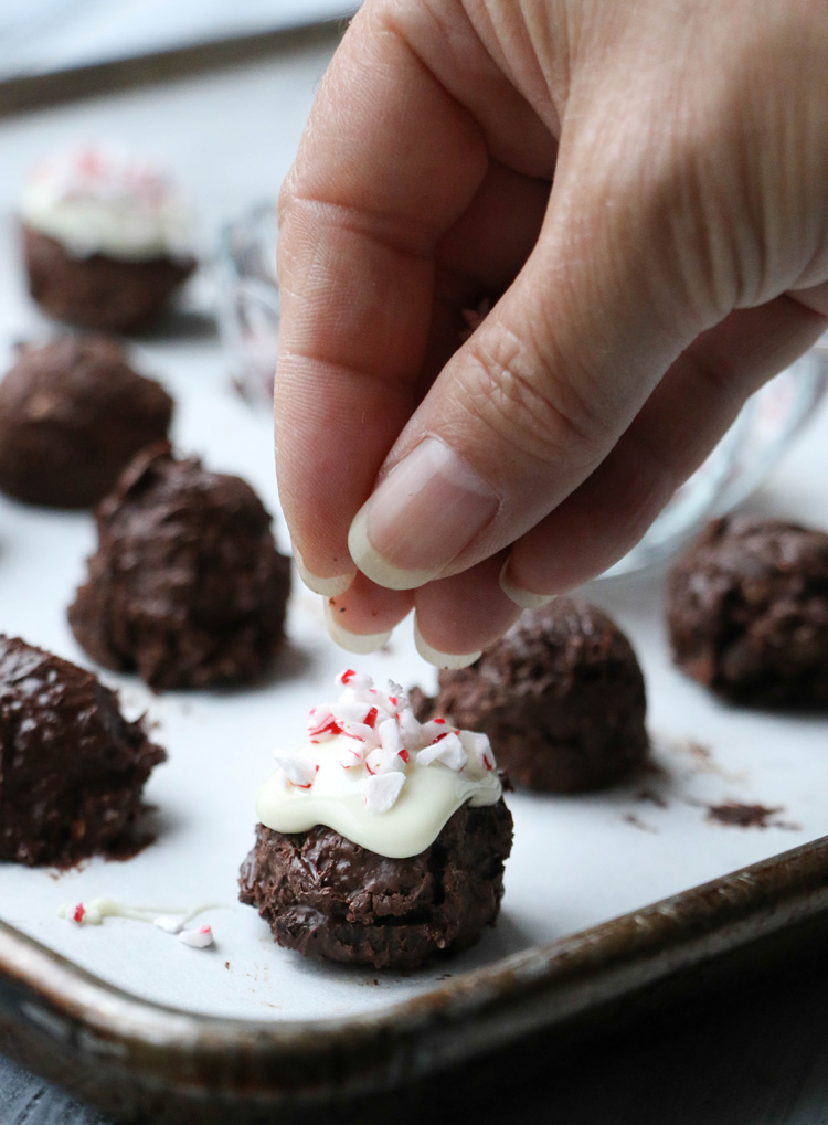 Sprinkling crushed peppermint candy on to a Peppermint Cookie Cluster on a baking sheet.