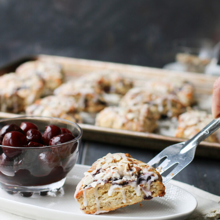 Placing a Cherry Almond Scone on to a white plate with a silver spatula.