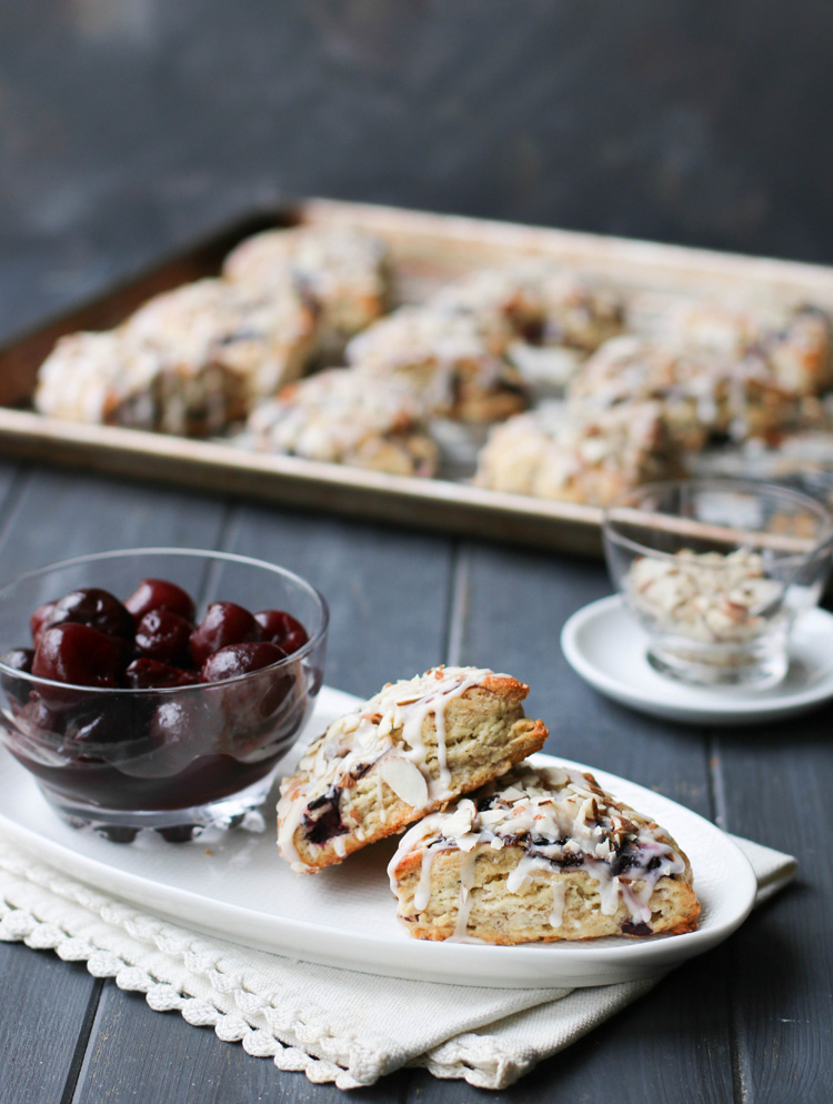 Cherry Almond Scones opened up on a white plate with a bowl of cherries.