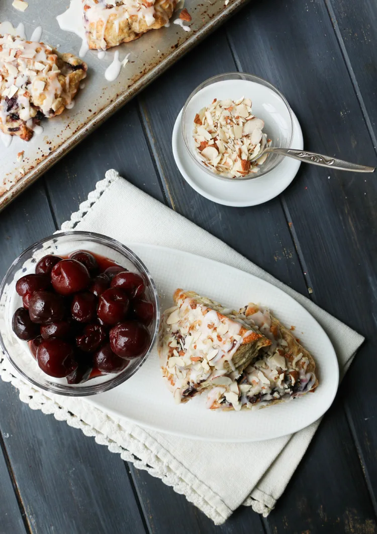An overhead photo of Cherry Almond Scones on a white plate with a bowl of cherries with a side dish of sliced almonds.