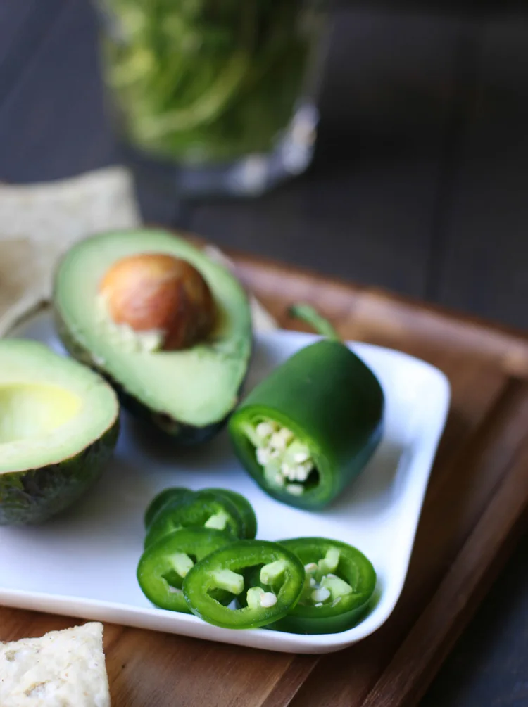 a sliced avocado and sliced jalapeno on a square white plate.