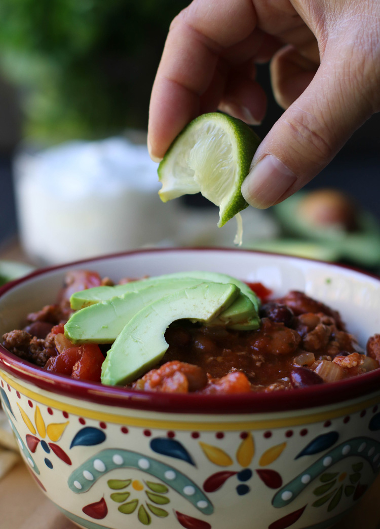 Squeezing a lime onto a bowl of Turkey Chili topped with slices of avocado.
