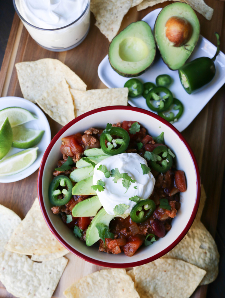An overhead photo of a bowl of Big Batch Turkey Chili topped with slices of avocado, jalapeno, sour cream and cilantro.
