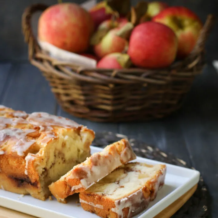 Sliced Apple Fritter Bread on a white plate in front of a basket of apples.