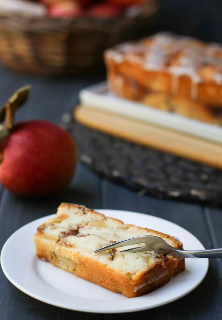 Once slice of Apple Fritter Bread on a white plate with a fork cutting into it.